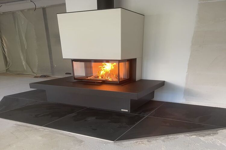 Moderner Kamin mit Glasfront und brennendem Feuer auf schwarzem Fliesenboden im Wohnraum.