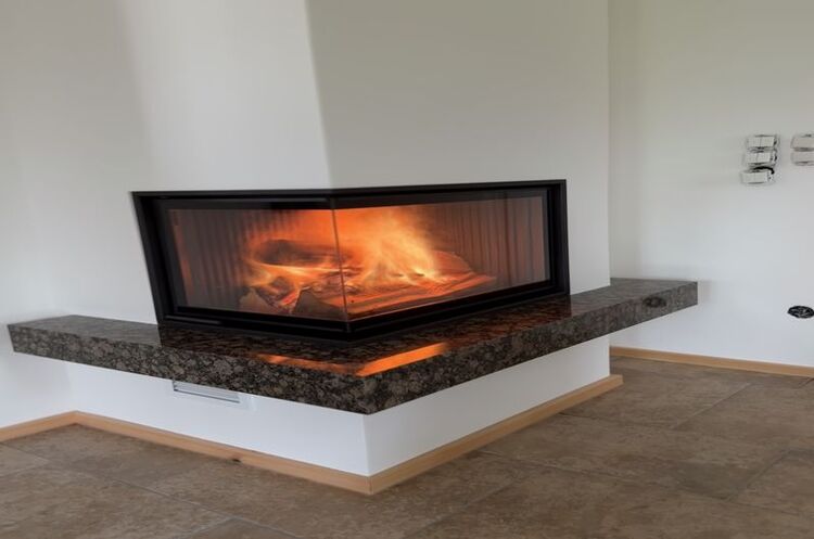 Moderner Eckkamin mit Glasfront und brennendem Feuer auf Marmorplatte im Wohnzimmer.
