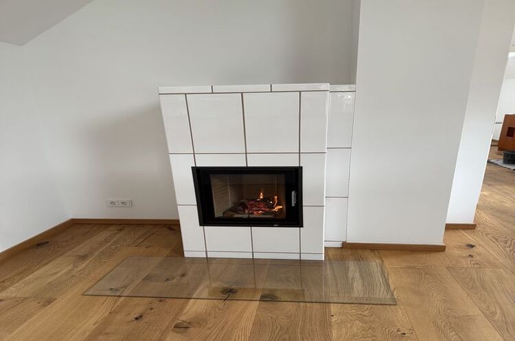 Moderner Kaminofen mit weiß gefliester Verkleidung auf Parkettboden im Wohnzimmer.